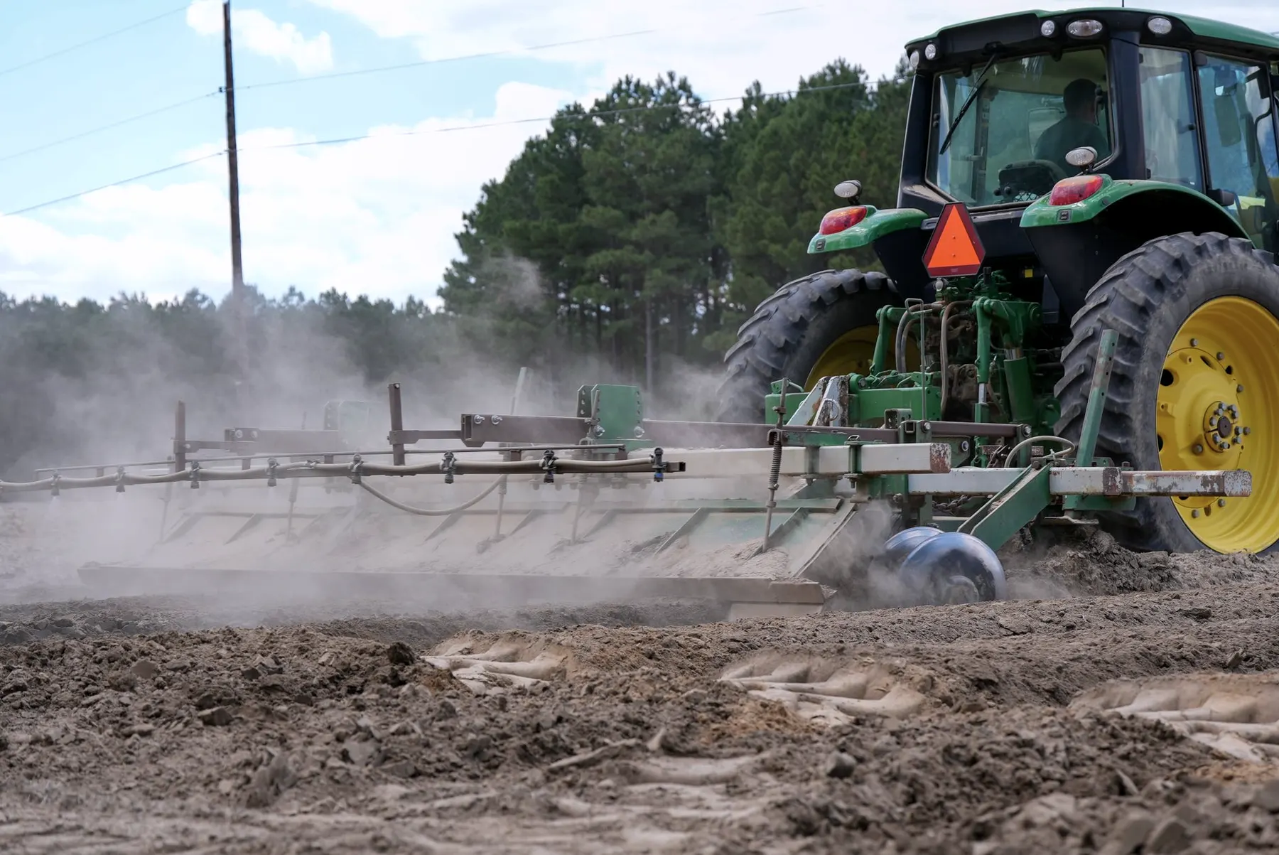 Tractor met aangekoppelde cultivator aan de rand van een veld
